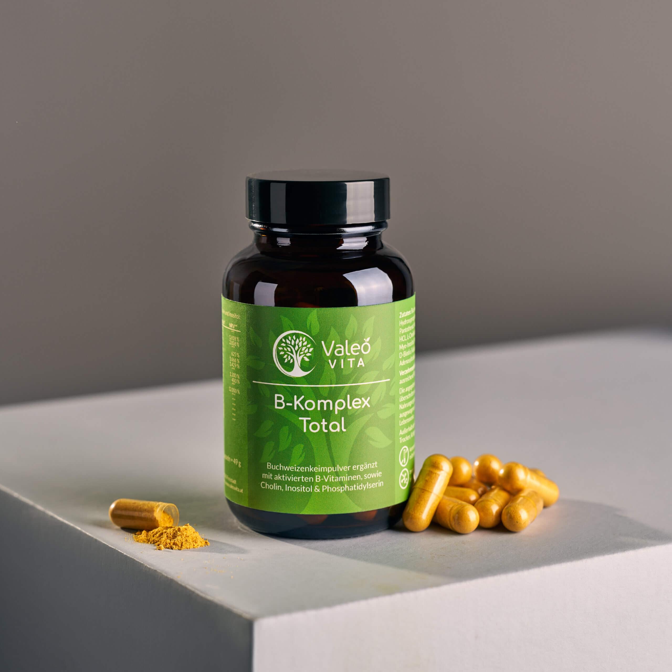Valeo Vita B-Komplex Total Kapseln in Braunglasdose mit gelben Kapseln und geöffnetem Kapselinhalt auf hellem Podest