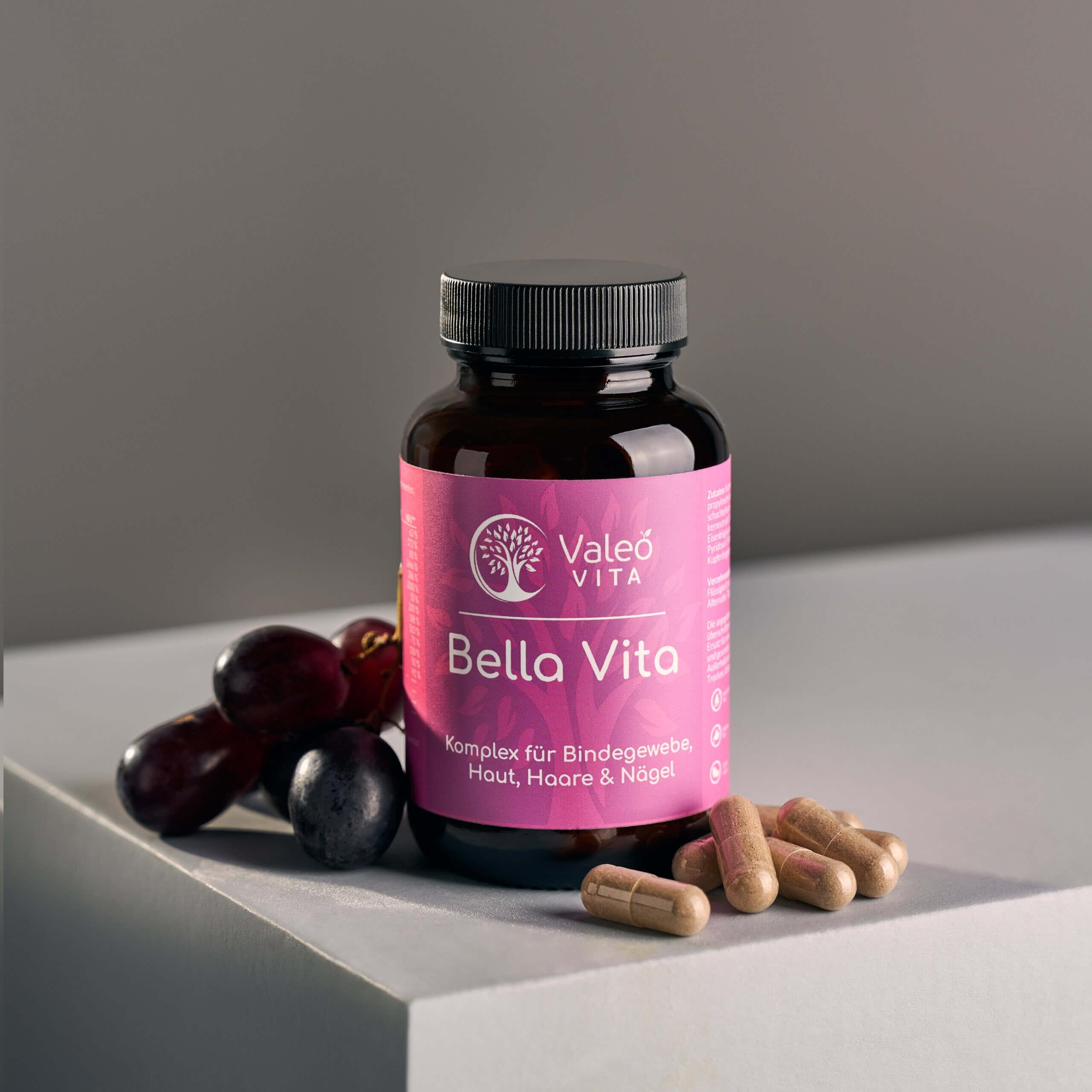 Valeo Vita Bella Vita Kapseln in Braunglasflasche mit Trauben auf grauem Podest