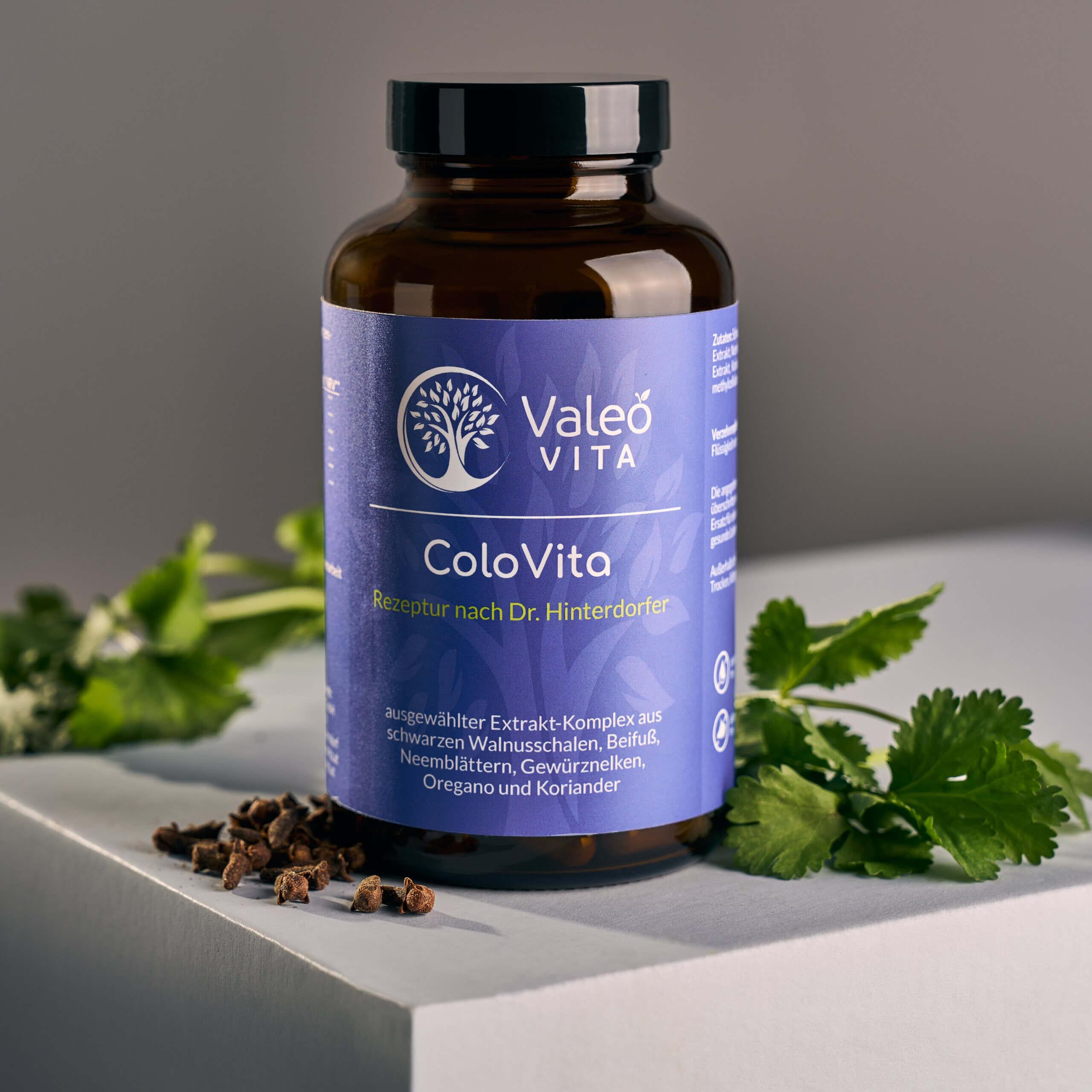 Valeo Vita ColoVita Kapseln in brauner Glasdose mit Pflanzenblättern und Gewürznelken auf hellem Podest