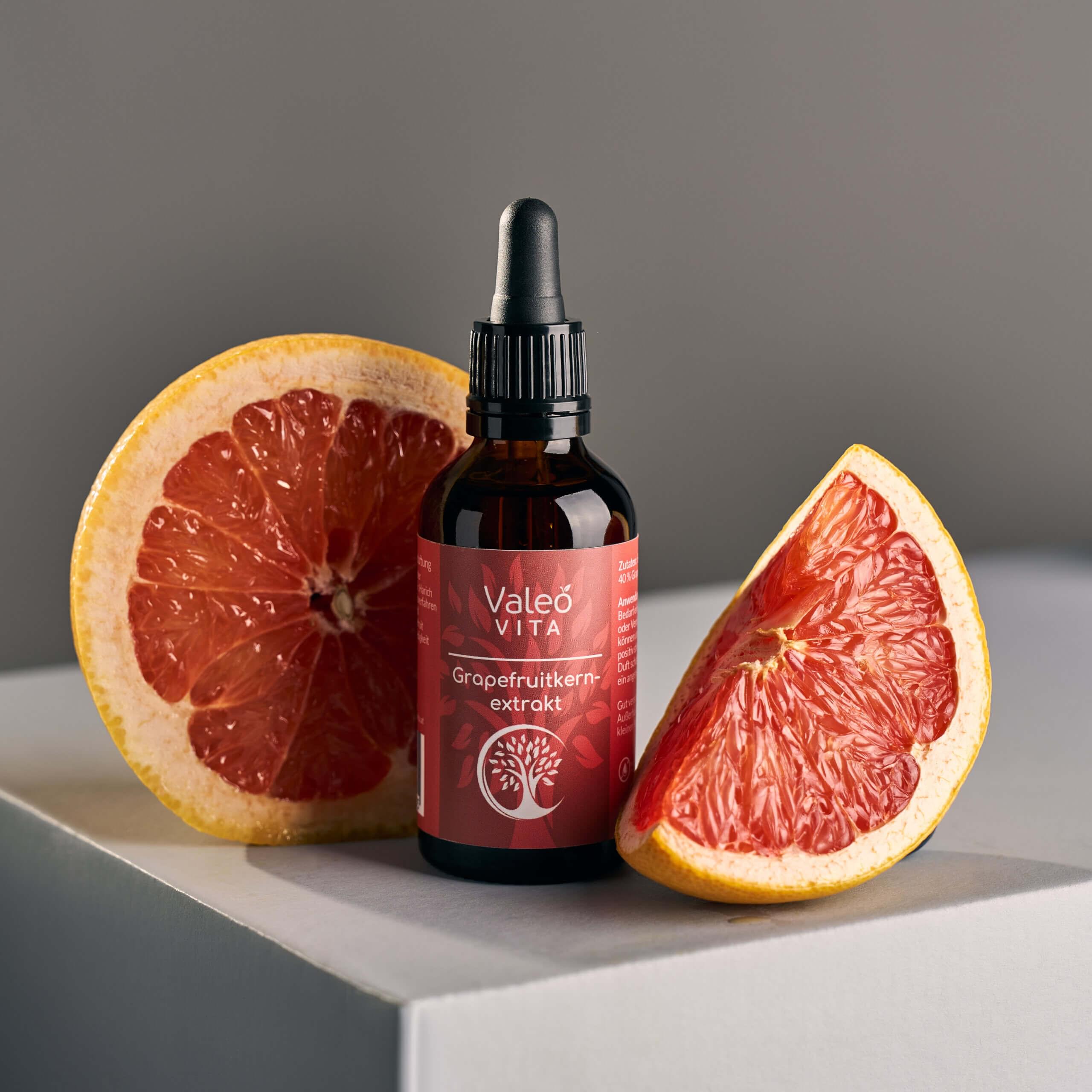 Valeo Vita Grapefruitkernextrakt in Braunglasflasche mit Pipette, platziert zwischen zwei aufgeschnittenen Grapefruits