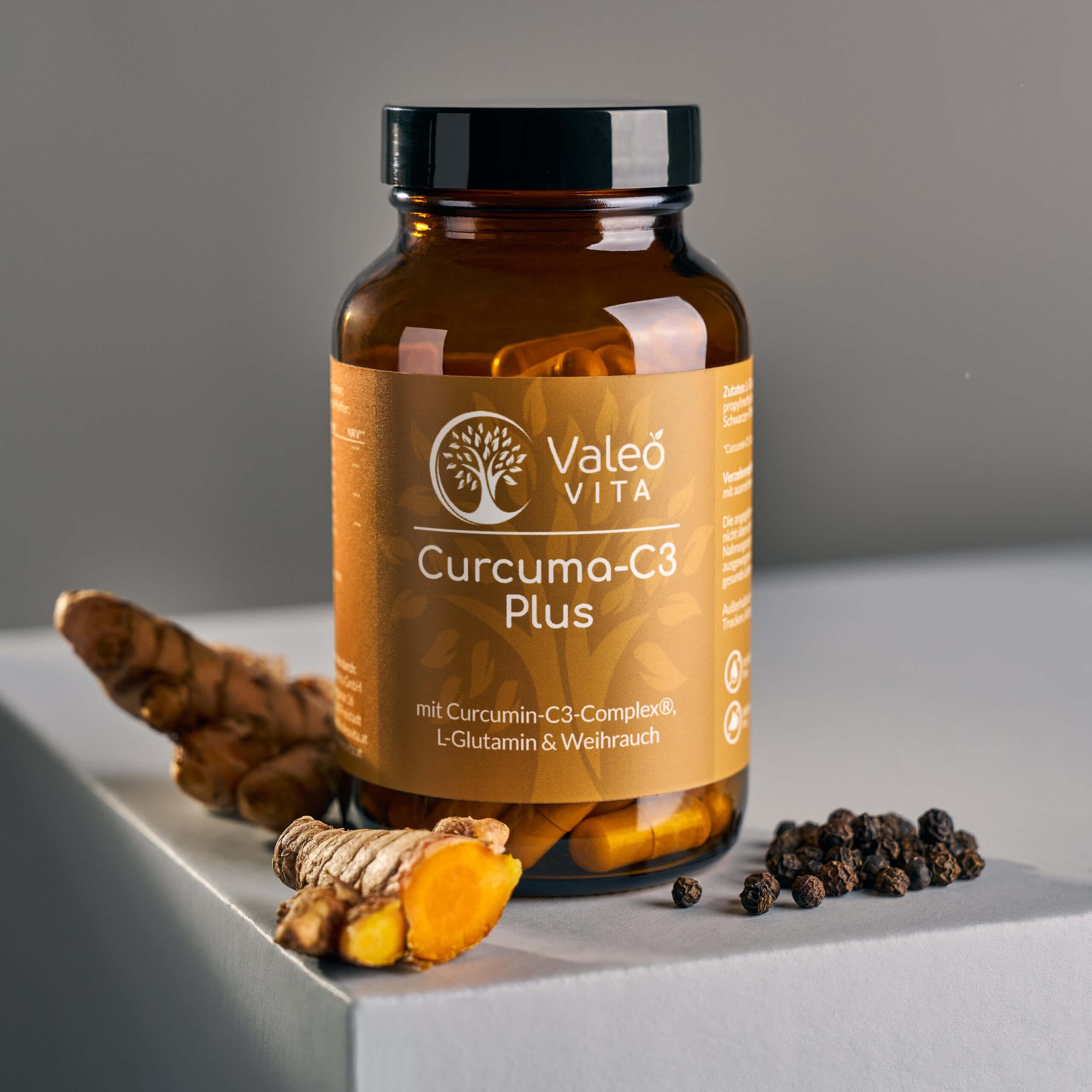 Valeo Vita Curcuma-C3 Plus Kapseln in Braunglasdose mit Kurkumawurzel und Pfefferkörnern auf neutralem Hintergrund