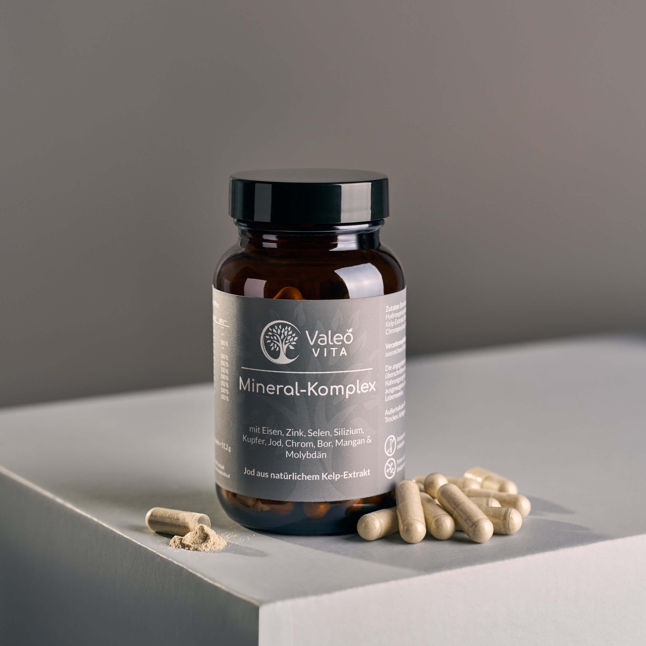 Valeo Vita Mineral-Komplex Kapseln in Braunglasdose mit beigen Kapseln und geöffnetem Kapselinhalt auf hellem Podest
