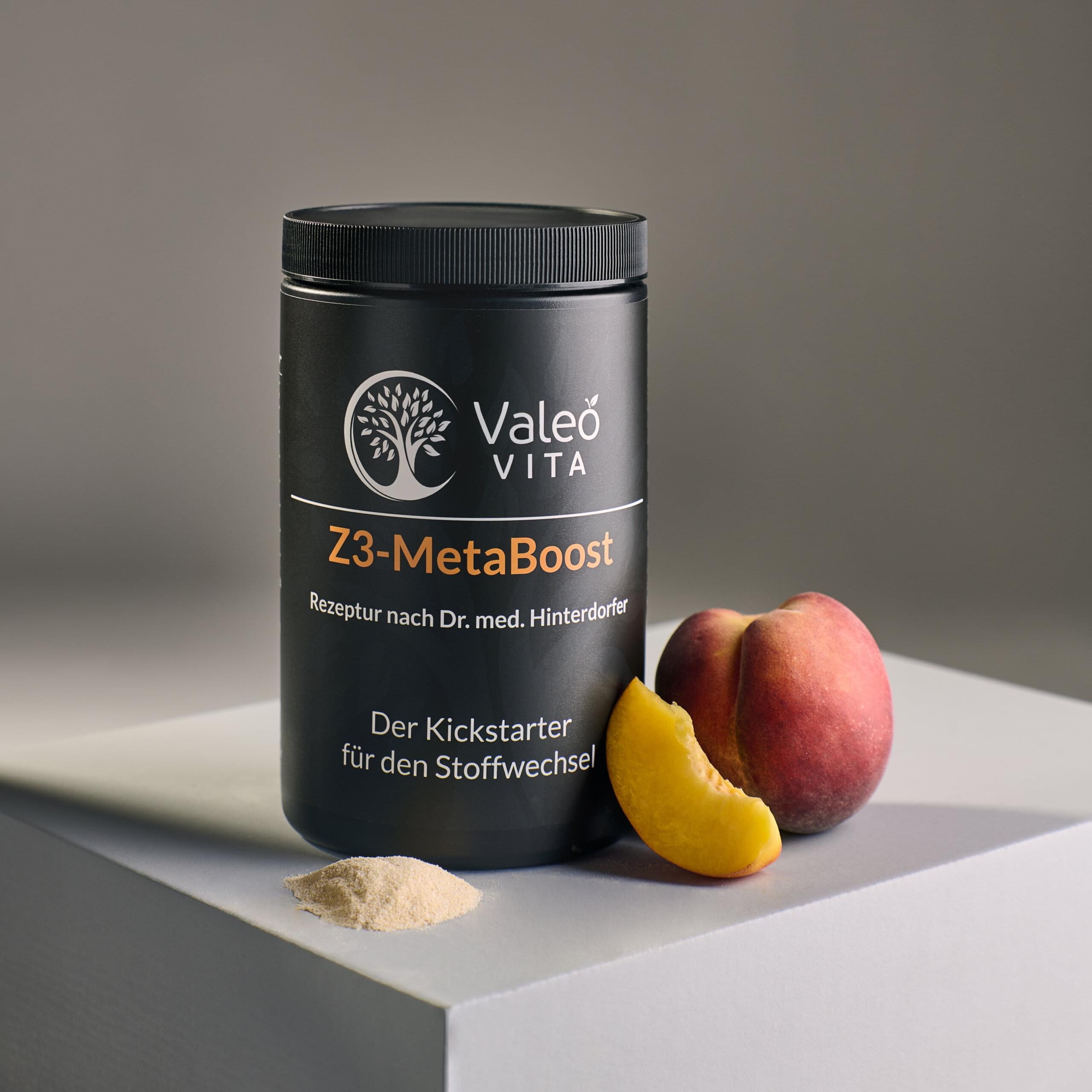 Valeo Vita Z3-MetaBoost Pulver in schwarzer Dose mit Pfirsich und Pulver auf Podest vor neutralem Hintergrund